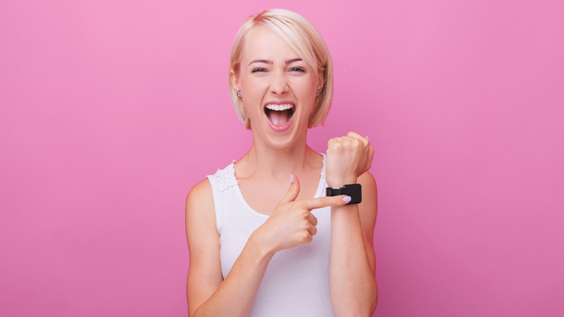 Mulher loira feliz com o seu smartwatch em fundo rosa, foto de estúdio
